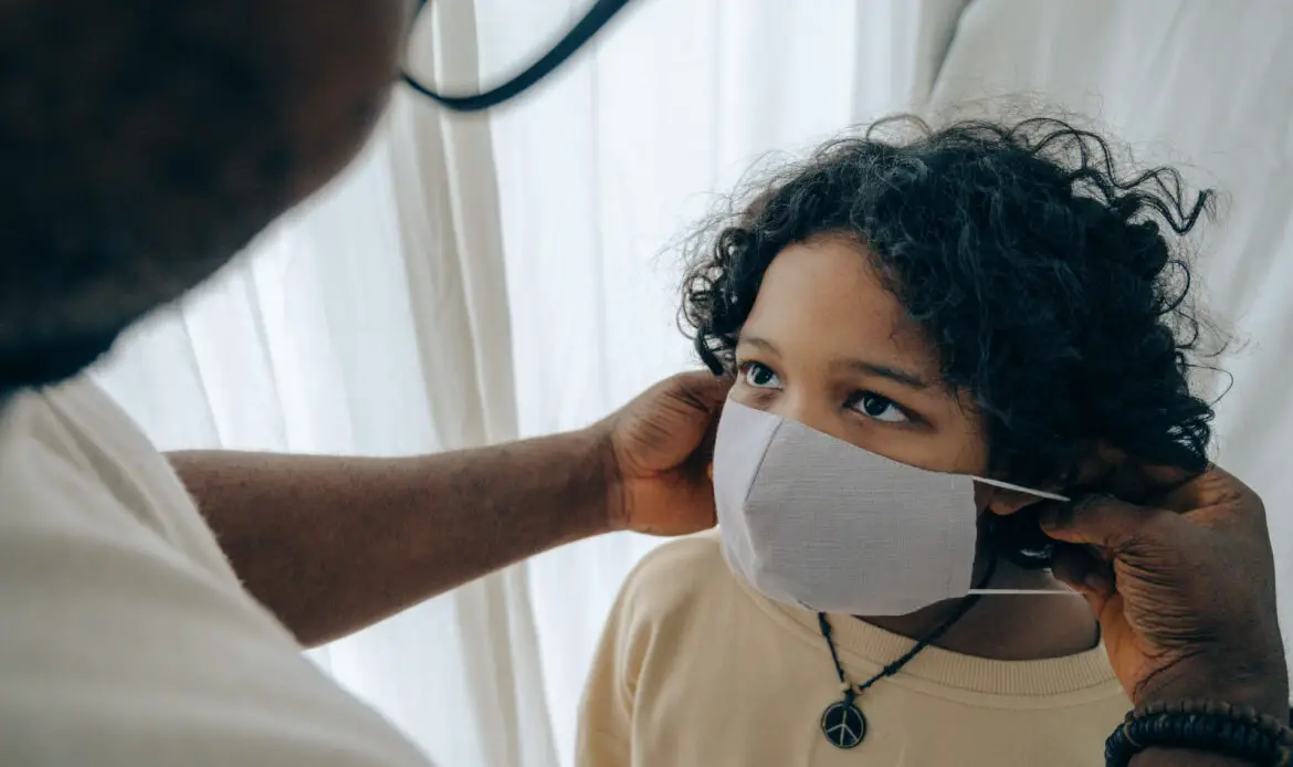 Crop man putting medical mask on face of ethnic child