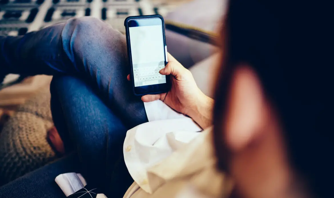 Back view of male checking banking balance on mobile phone connected to home internet, millennial man using smartphone for messaging with followers via modern application during free time for chatting