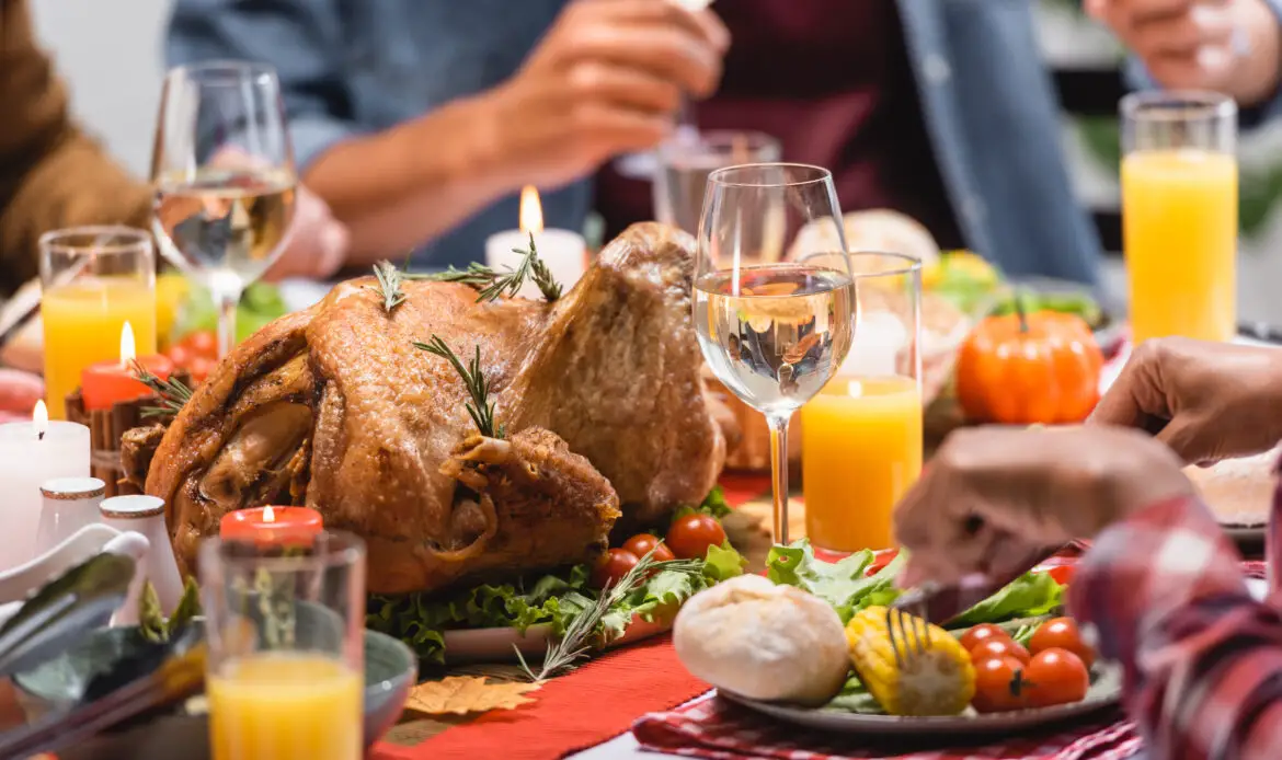 Cropped view of turkey with drinks and candles on table near multiethnic family celebrating thanksgiving