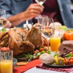 Cropped view of turkey with drinks and candles on table near multiethnic family celebrating thanksgiving