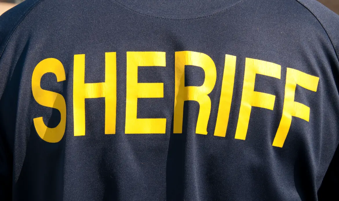 Closeup image of a back of a sheriff's deputy, with text sheriff in yelllow letters