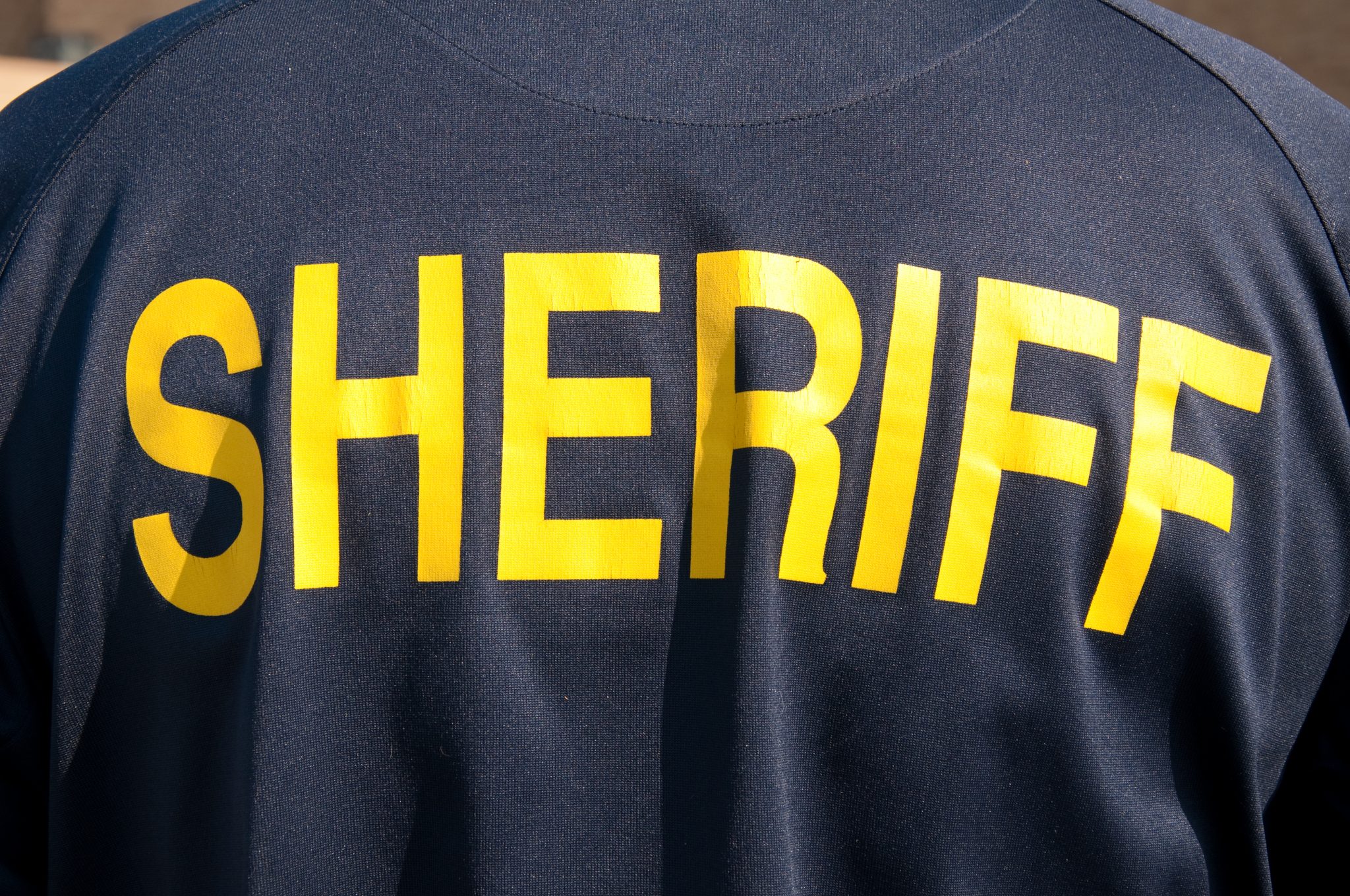 Closeup image of a back of a sheriff's deputy, with text sheriff in yelllow letters