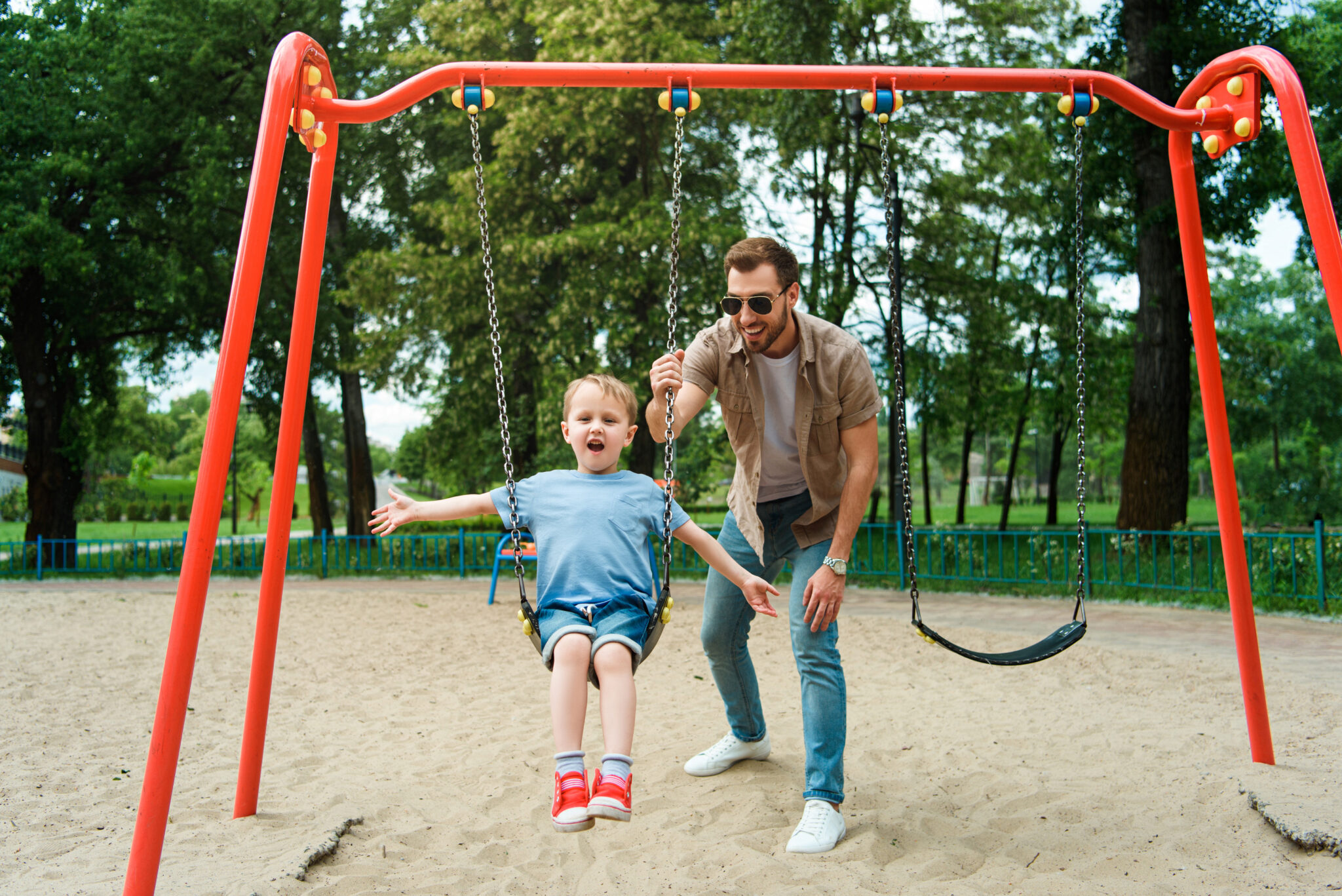 father and son having fun on swing at playground in park