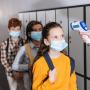 Teacher using infrared thermometer on pupil in medical mask near kids on blurred background