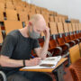 Man student in grey t-shirt sitting in face mask in empty university classroom