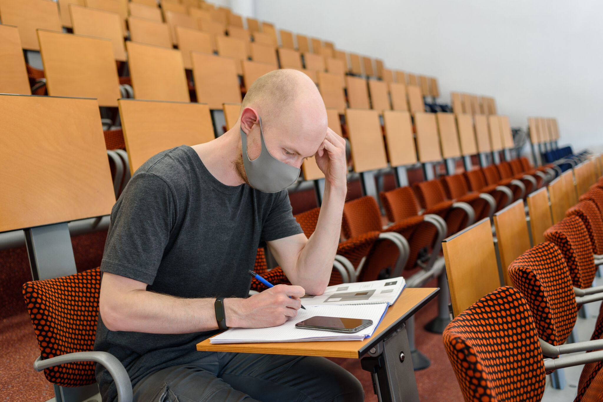 Man student in grey t-shirt sitting in face mask in empty university classroom