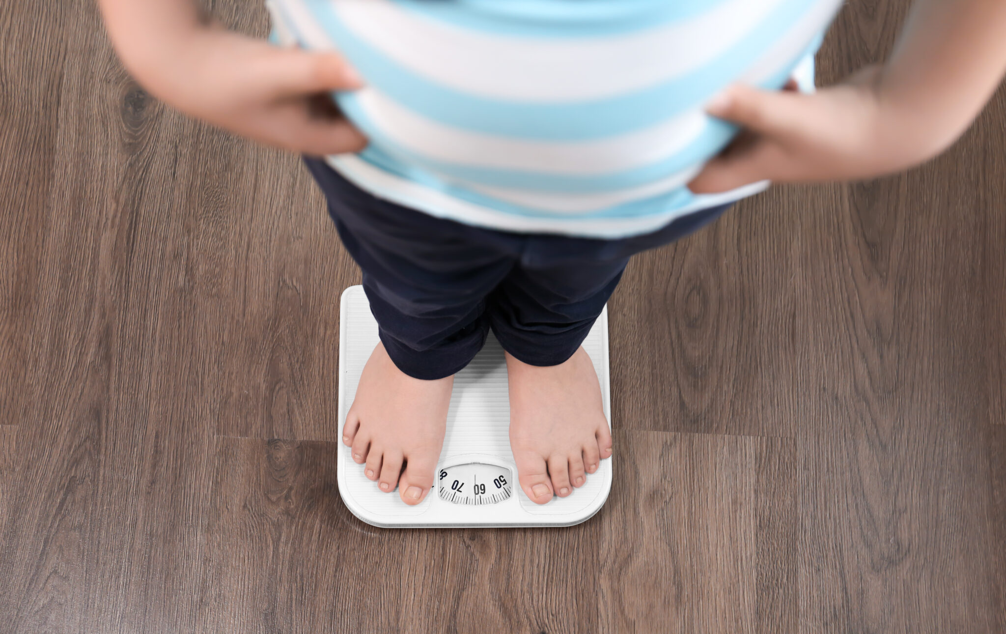 Overweight boy standing on floor scales indoors