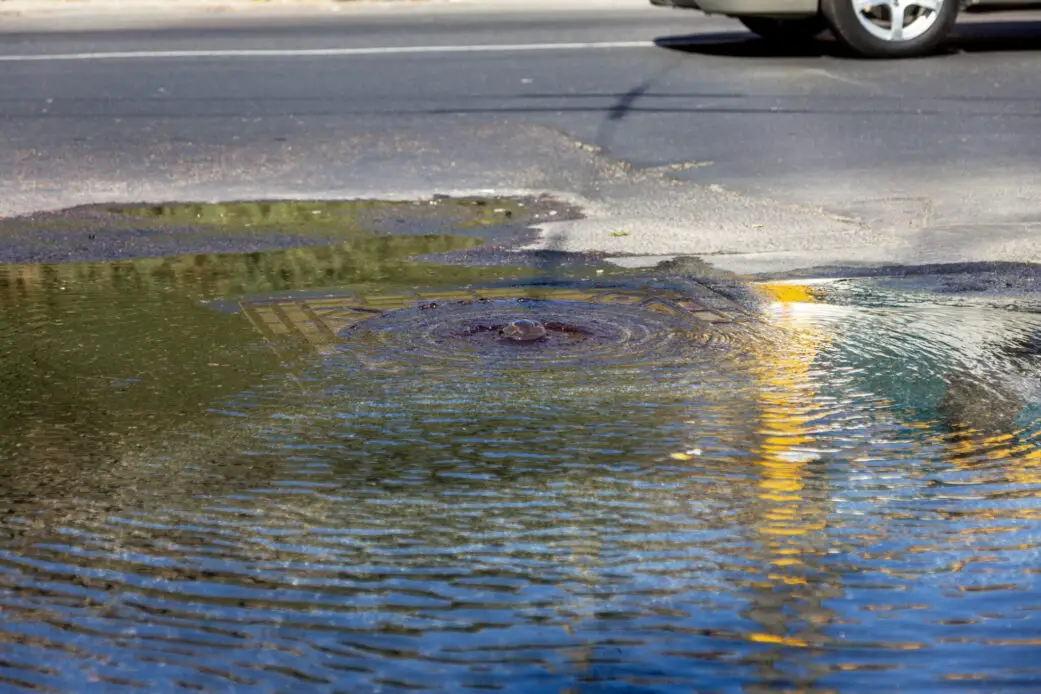 Accident of water supply, sewerage. Water flows from hatch of road sewage system. Dirty sewer flows down fountain along road. Water flows from hatch. Fountain flows down road from sewer