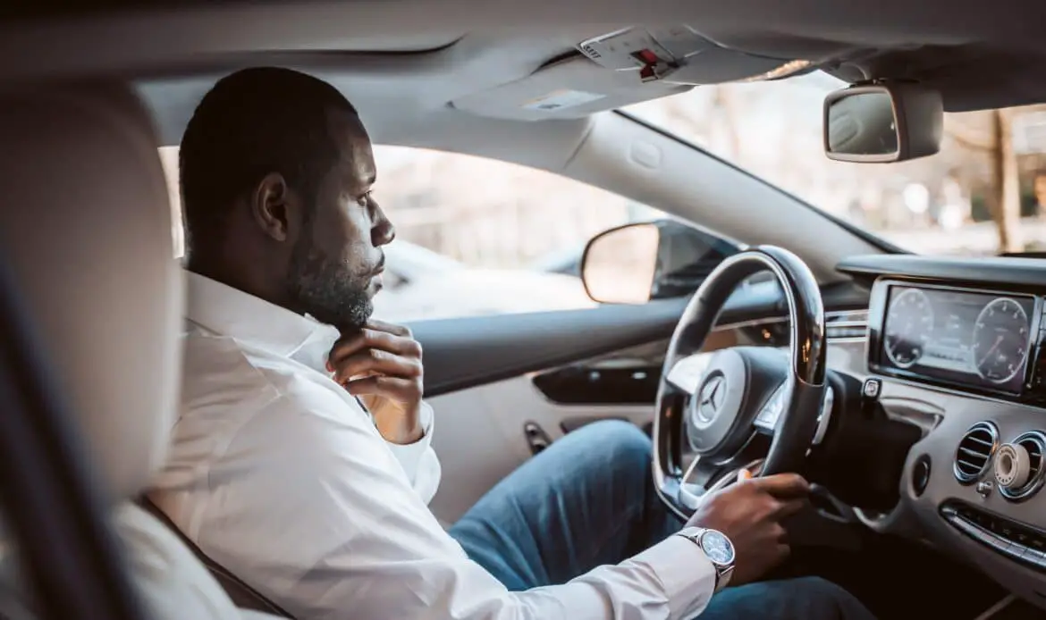 Fortune Vieyra dressed in business casual clothing and sitting in a Mercedes with a hand steering wheel.