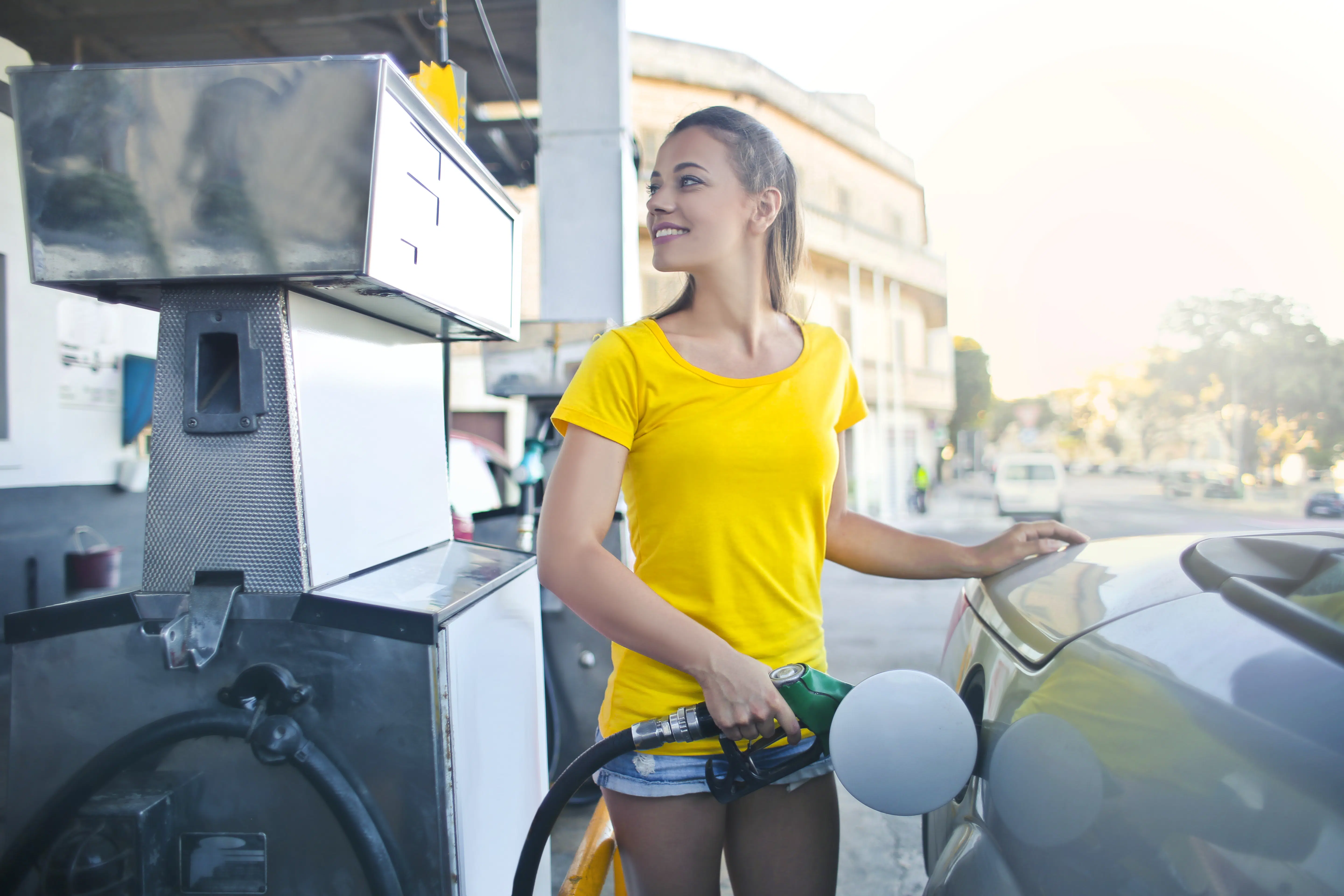 Woman in yellow shirt while filling up her car with gasoline