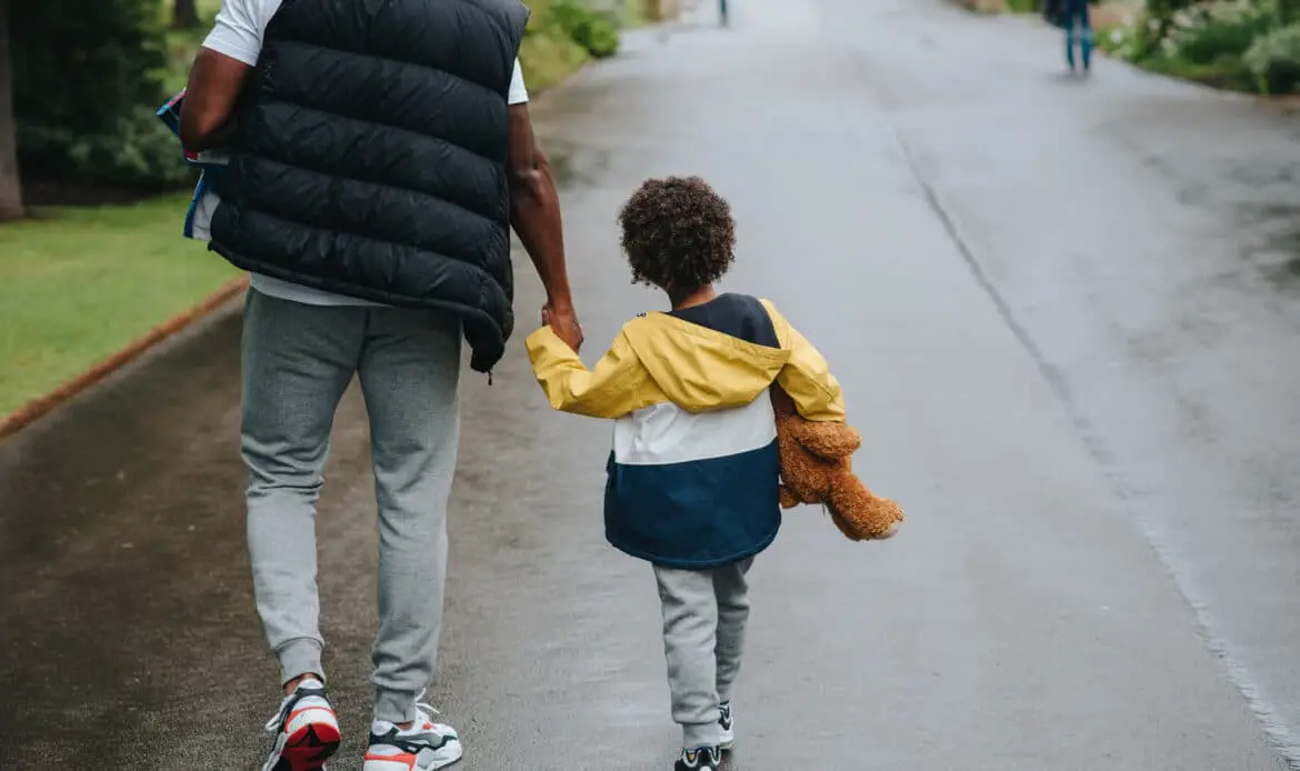 Crop black man with son holding hands strolling on roadway