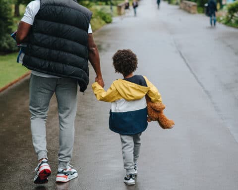 Crop black man with son holding hands strolling on roadway