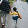 Crop black man with son holding hands strolling on roadway