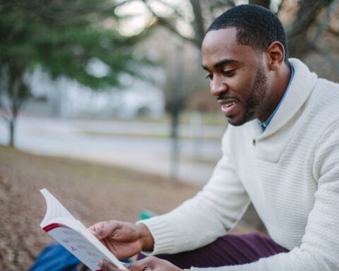 Selective Focos Photography of Man in White Sweater Reading Book