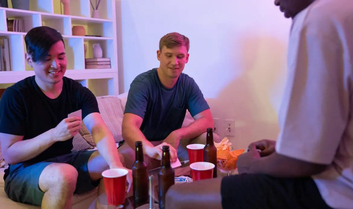 Group of friends playing cards and drinking beer in a cozy living room setting.