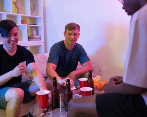 Group of friends playing cards and drinking beer in a cozy living room setting.