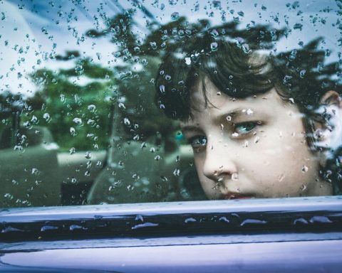 A child gazes contemplatively through a rain-marked car window, capturing a moment of introspection.