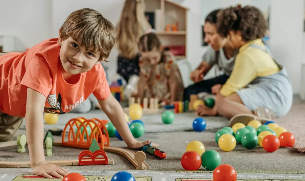 Happy children and a caregiver playing with colorful toys in a lively indoor playroom setting.