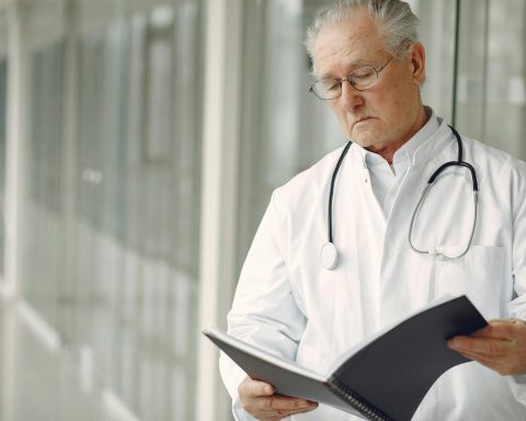 Elderly doctor with stethoscope attentively reading a medical report in a modern hospital setting.