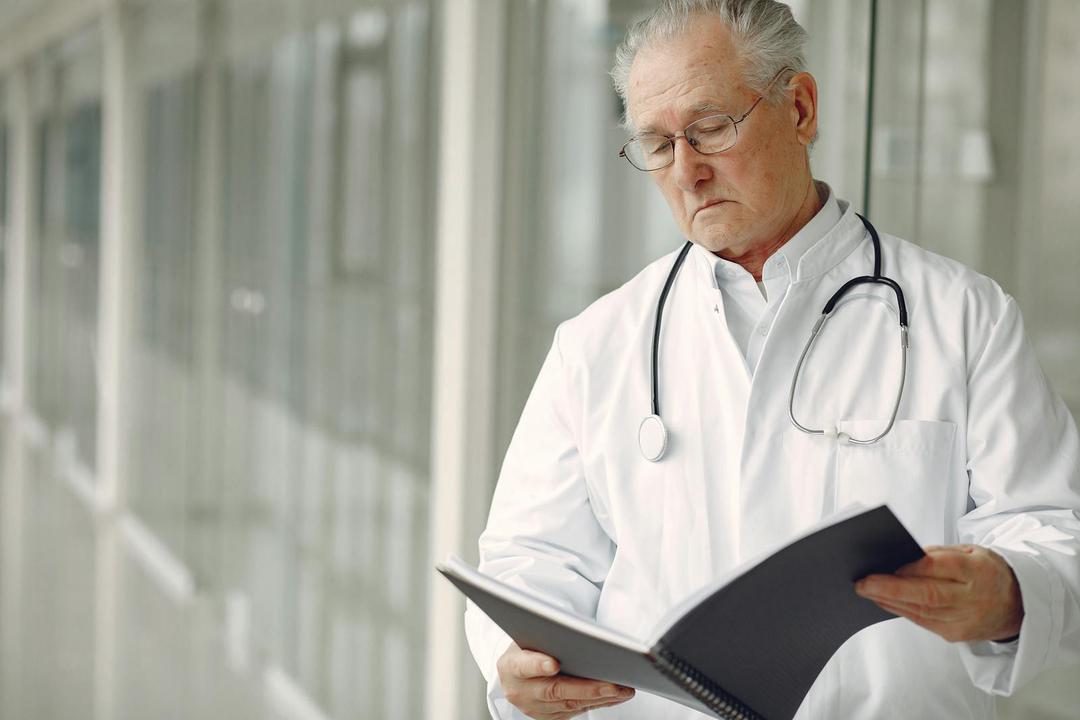 Elderly doctor with stethoscope attentively reading a medical report in a modern hospital setting.