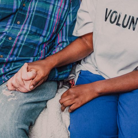 A volunteer holding hands with a senior, symbolizing care and community support.