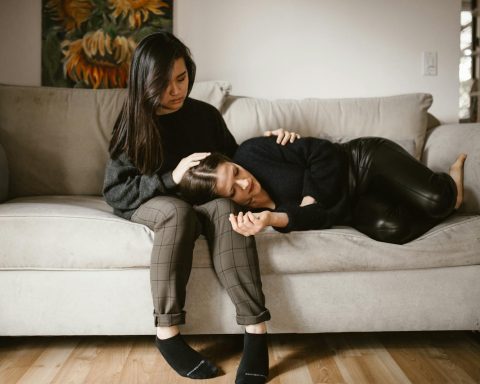 A comforting scene of empathy and support between two women sitting on a sofa indoors.