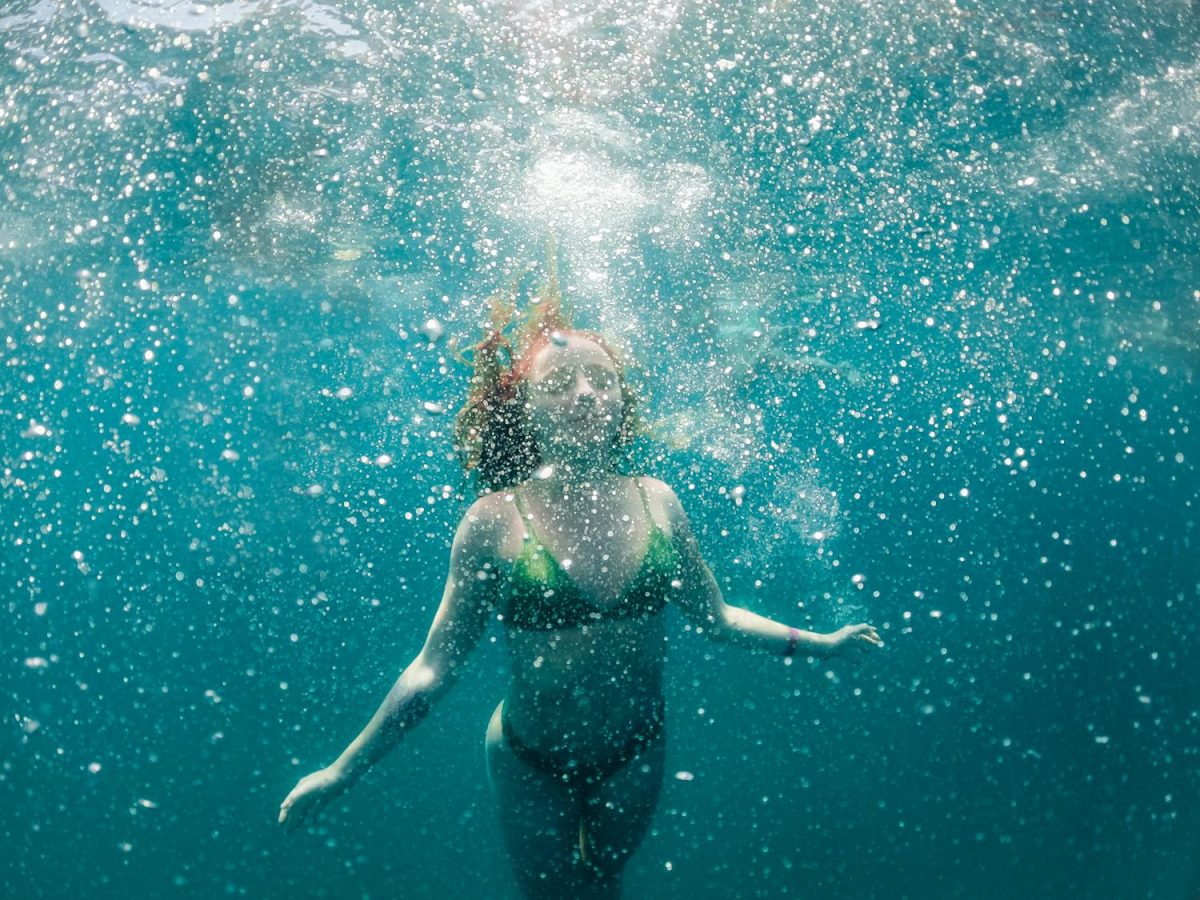 Woman in a bikini diving underwater surrounded by bubbles in a sea setting.