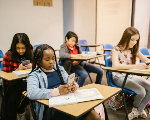 A group of four students in a classroom using smartphones and notebooks during a lesson.