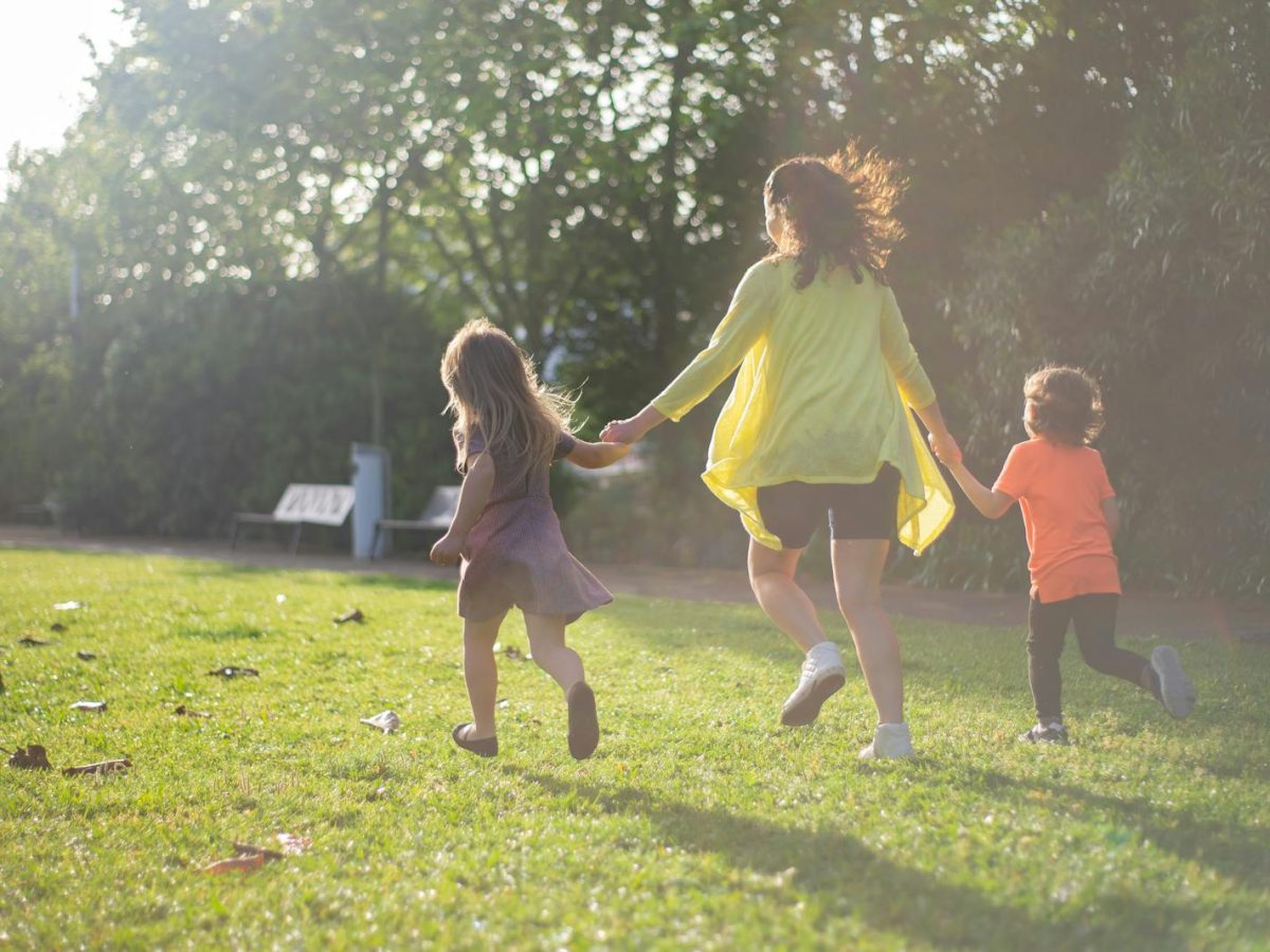A mother with two children running and playing in a sunny park, enjoying family time.