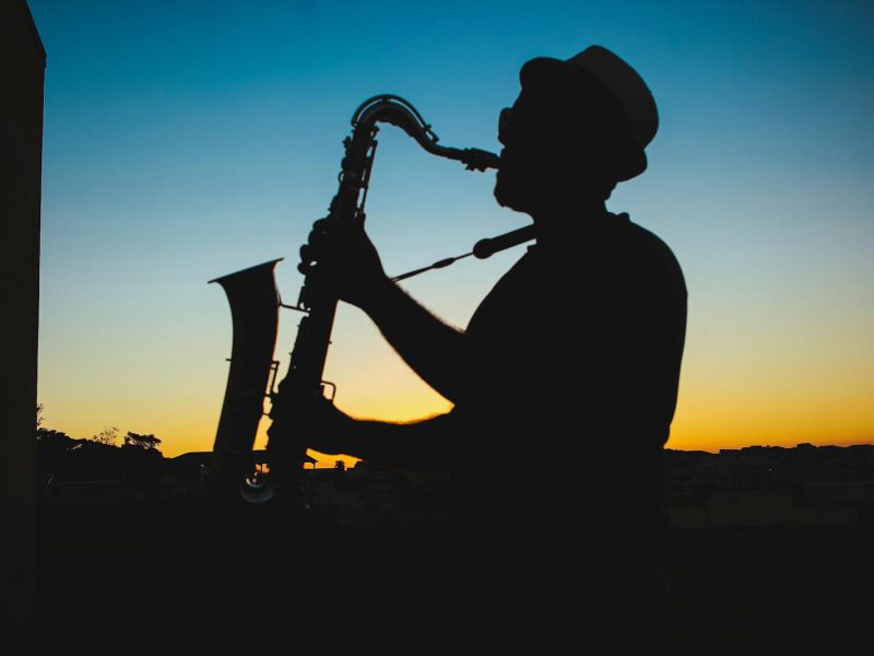 A man playing the saxophone silhouetted against a vibrant sunset sky.