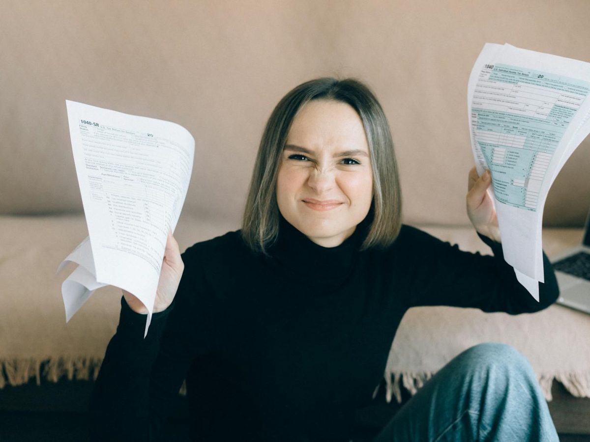 Frustrated young woman holding tax documents while sitting indoors.