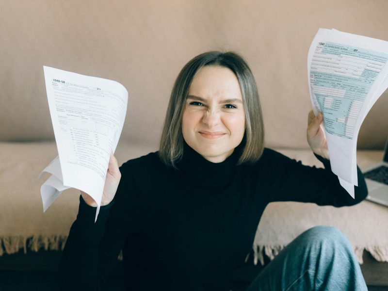 Frustrated young woman holding tax documents while sitting indoors.