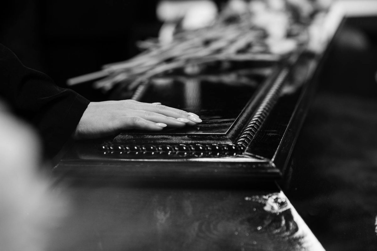 A woman's hand rests on a casket, conveying a poignant moment of farewell during a solemn funeral.