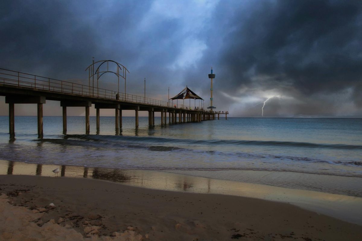 Dramatic storm over Brighton Jetty, Australia with dark clouds and lightning in the distance.