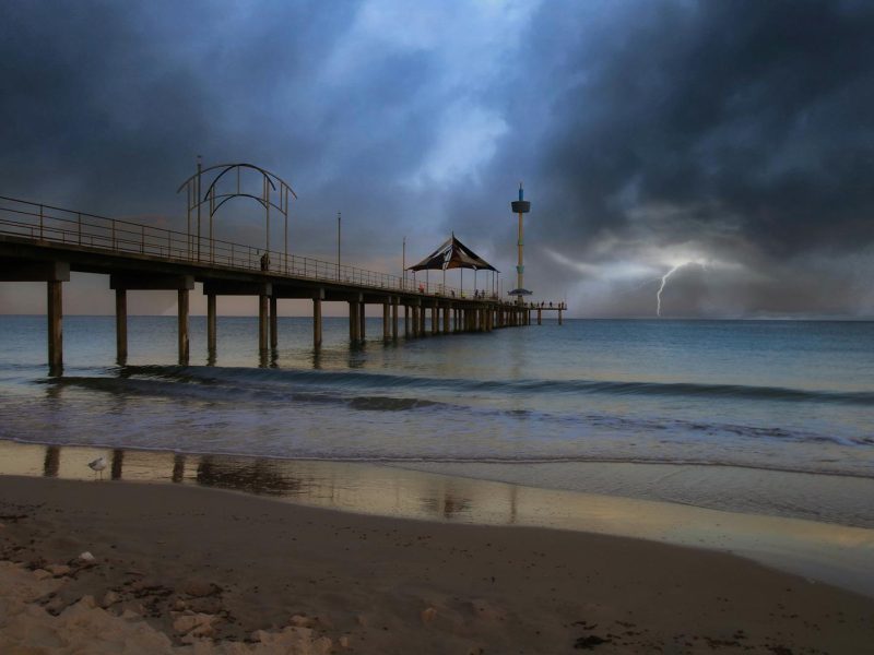 Dramatic storm over Brighton Jetty, Australia with dark clouds and lightning in the distance.