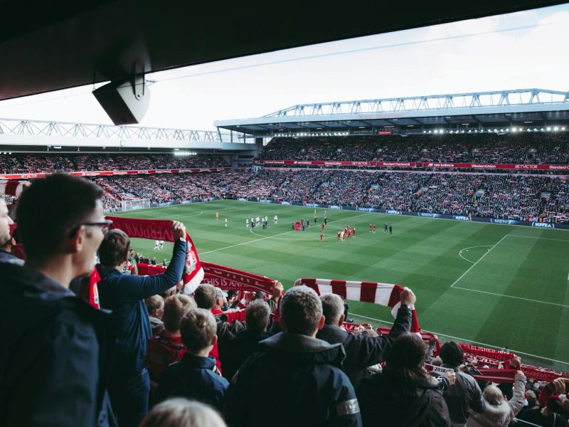 Fans cheer as players take the field at a vibrant football stadium, creating an electric atmosphere.