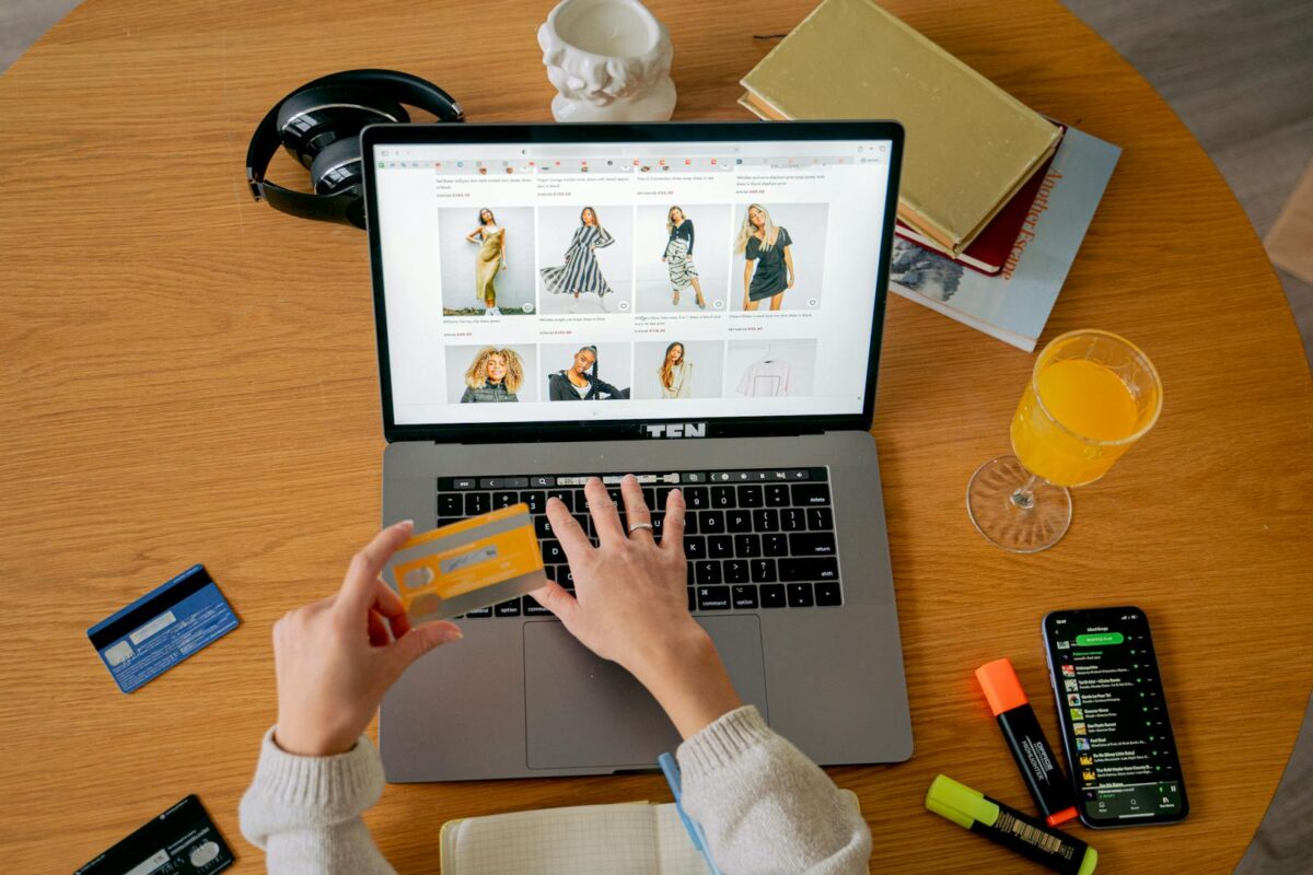 Hands holding credit card making online purchase on laptop at wooden desk with various items.