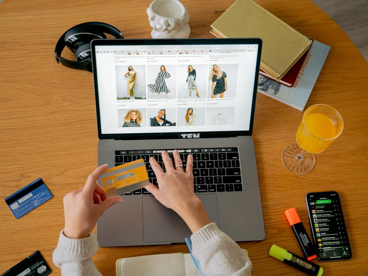 Hands holding credit card making online purchase on laptop at wooden desk with various items.
