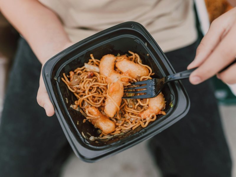 Tasty Asian noodles with shrimp in a black container held by a person.