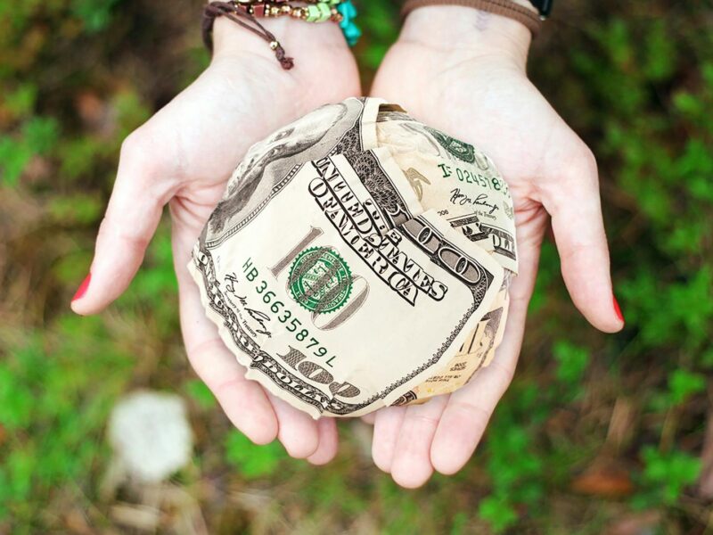 Hands holding crumpled money outdoors, symbolizing charity and financial support.