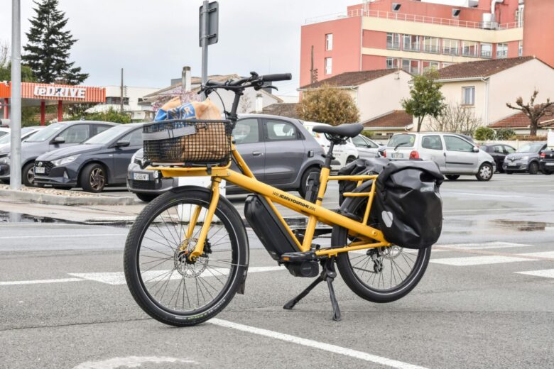 A yellow cargo e-bike carrying groceries parked outside a supermarket in France.