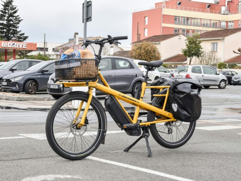 A yellow cargo e-bike carrying groceries parked outside a supermarket in France.