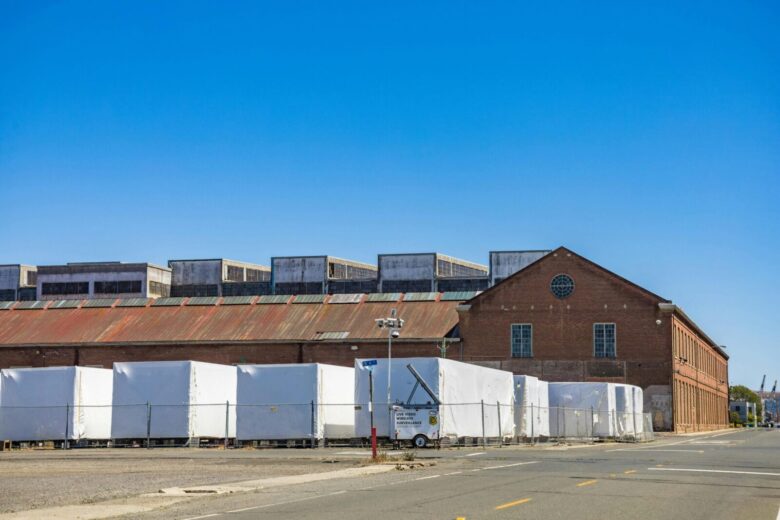 A brick warehouse with white covered storage against a clear blue sky on an empty street.