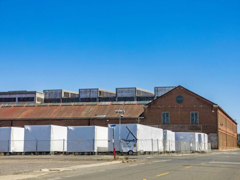 A brick warehouse with white covered storage against a clear blue sky on an empty street.