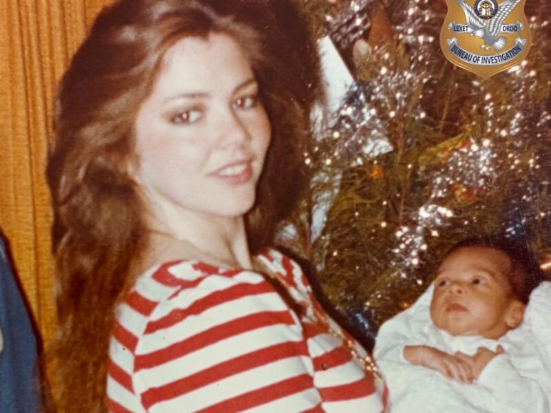 A woman with long brown hair wearing a red and white striped shirt is holding a baby wrapped in a white blanket. The background includes a decorated Christmas tree with tinsel. In the top right corner, there is a badge emblem that reads "State of Georgia Bureau of Investigation.
