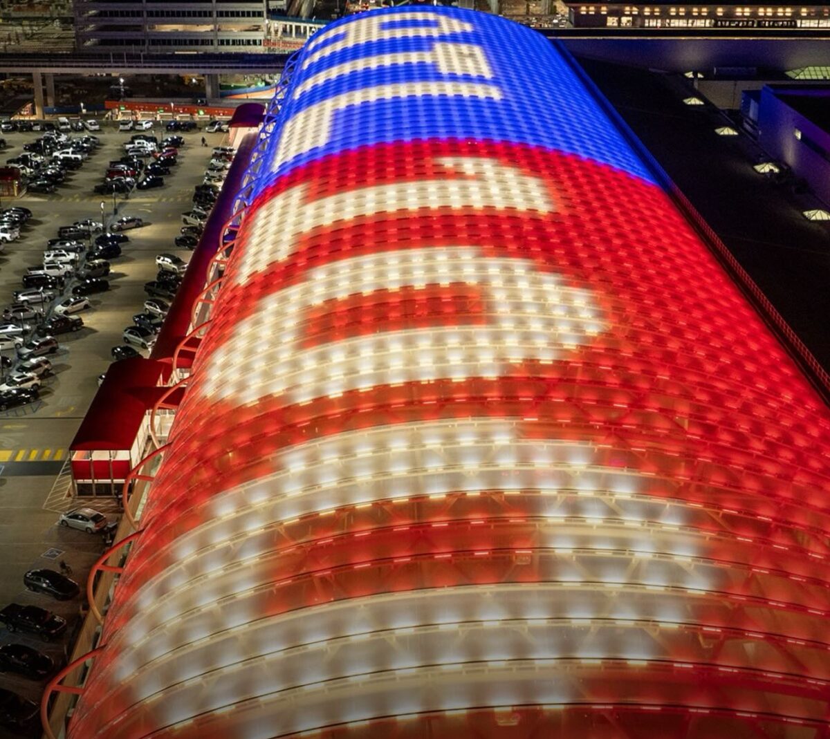 A large, curved building roof illuminated at night with red, white, and blue lights forming the words "ATL" and "ATLANTA" in a bold, stylized font. The surrounding area includes a parking lot filled with cars and other buildings in the background. The bottom left corner features the text "ATL Pic of the Week" in red and yellow.