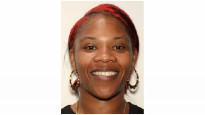 Close-up of a smiling woman with red hair styled back, wearing large gold hoop earrings and a black top.
