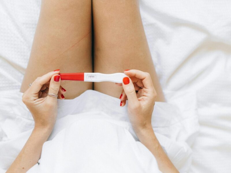 A close-up of a woman's hands holding a positive pregnancy test with two lines.