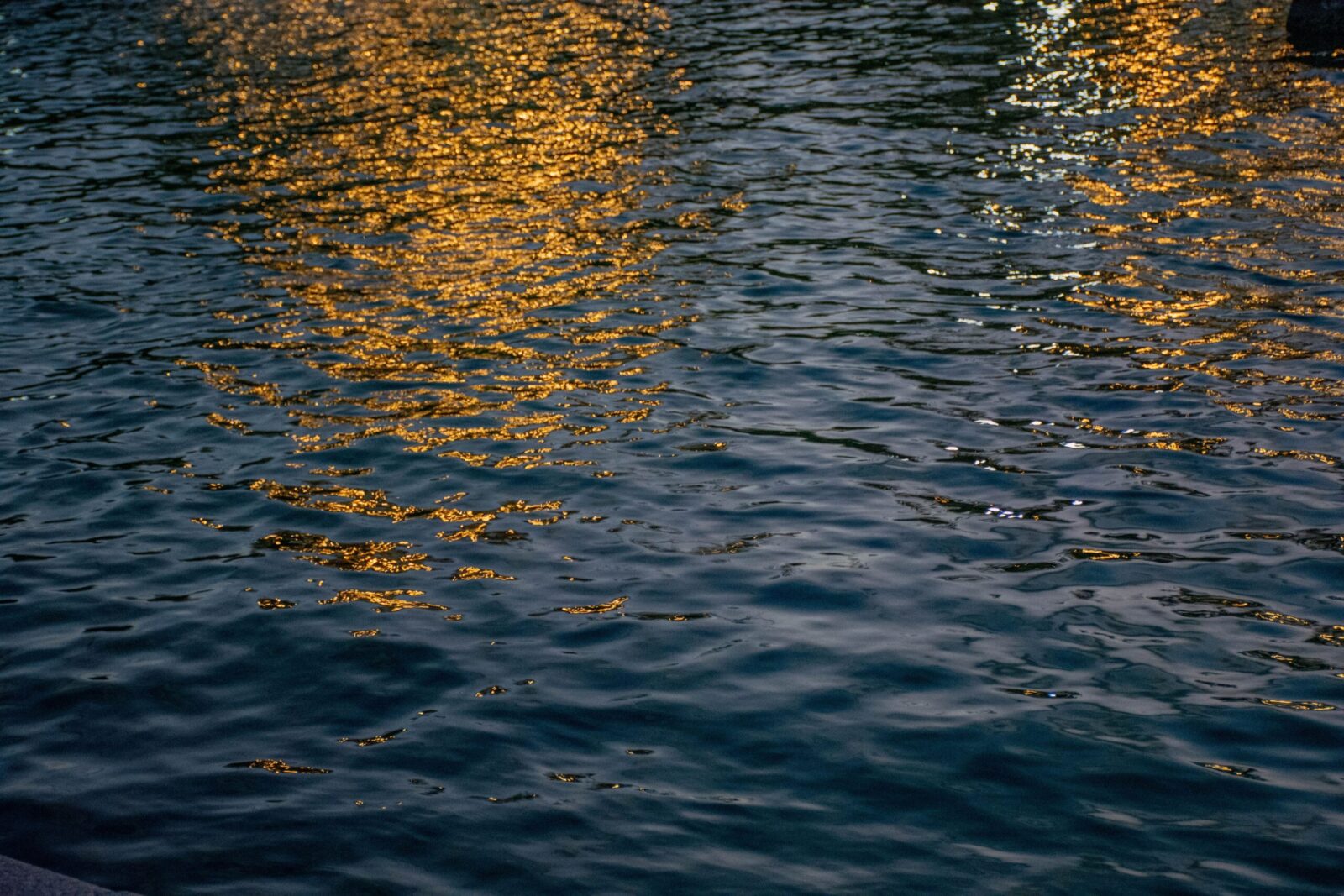 Evening lights reflecting on a tranquil water surface, creating a serene golden glow.