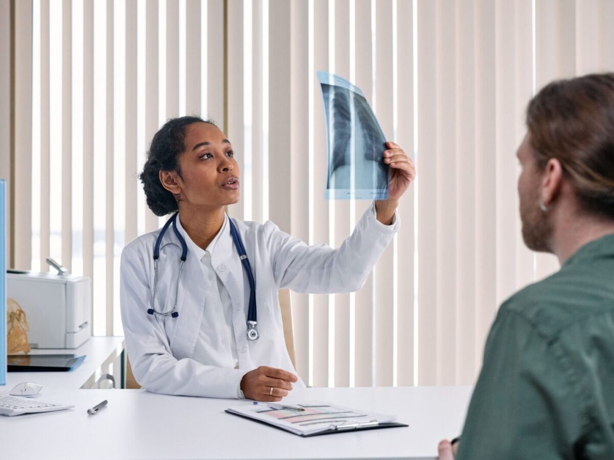 Female doctor examines x-ray results with male patient in a medical setting.